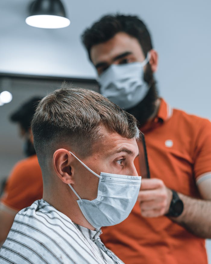 Side view of a barber cutting hair of a client wearing a face mask in a modern barbershop.